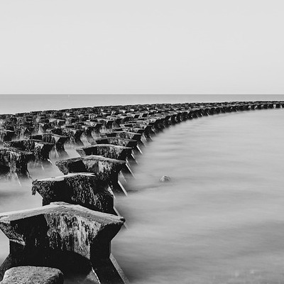 A black and white picture of the sea with short stone pillars in it.